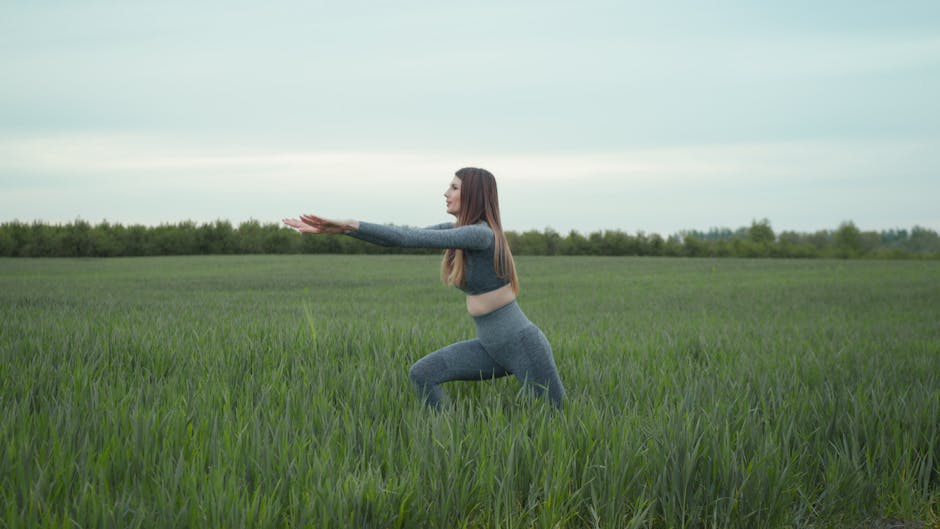 Woman practicing yoga in a green field, enjoying nature and freedom